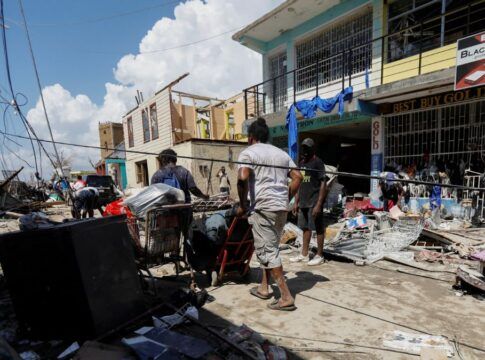 Homens empurram carrinhos com pertences em meio a rua destruída pelo furacão