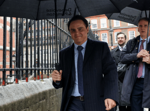 Felipe Massa veste terno e grava e segura um guarda-chuva caminhando pela calçada