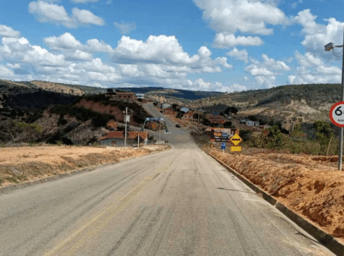 Radar de controle de velocidade instalado em rodovia de área rural, próximo a vegetação e montes, em um dia ensolarado.