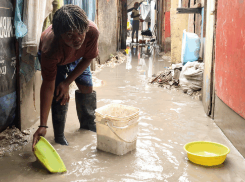 Mulher usa bacia para colher água do chão alagado numa rua estreia