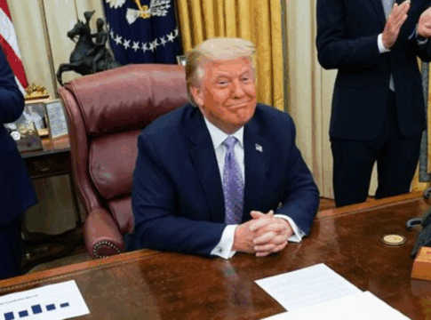 Donald Trump sentado à sua mesa na Casa Branca e sorrindo
