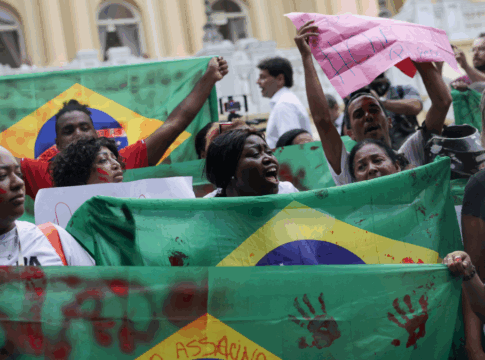 Pessoas erguem bandeiras do Brasil com marcas de mãos pintadas de vermelho em protesto