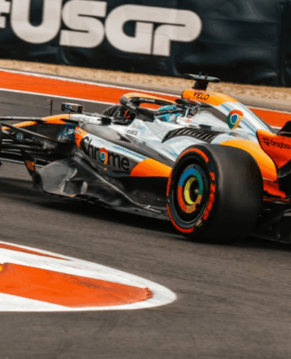 Carro de Fórmula 1 da Mclaren, laranja e prata, fazendo uma curva à esquerda.