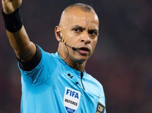 Árbitro Wilton Pereira Sampaio, com o braço direito aberto, uniforme azul FIFA.