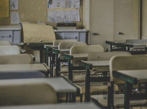 Uma sala de aula com cadeiras e mesas vazinhas, com estantes no fundo.