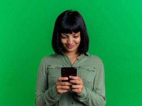 Mulher de cabelo preto com franja em um fundo verde segurando um celular