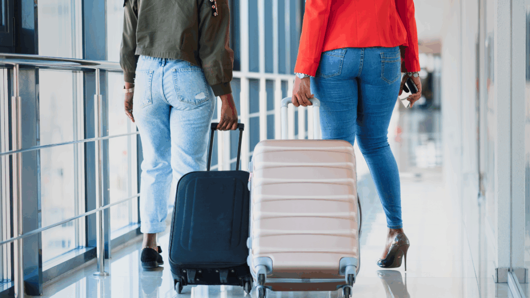 Duas mulheres caminham pelo aeroporto, cada uma puxando sua mala.