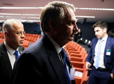 Imagem mostra o ex-presidente Jair Bolsonaro em audiência do julgamento da tentativa de golpe. Ele aparece no primeiro plano, com uma sombra que deixa apenas a silhueta do rosto dele. Atrás aparecem cadeiras da audiência.