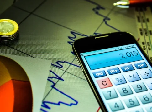 Foto de um celular, com o aplicativo da calculadora aberta, em cima de uma folha com um gráfico genérico