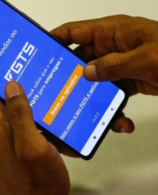 A imagem mostra as mãos de uma pessoa segurando o celular. Na tela do aparelho está o aplicativo do FGTS