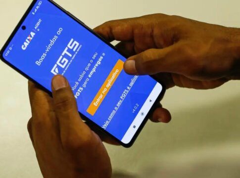 A imagem mostra as mãos de uma pessoa segurando o celular. Na tela do aparelho está o aplicativo do FGTS