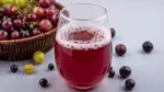 Copo de suco de uva, com várias uvas roxas no fundo