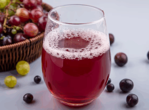 Copo de suco de uva, com várias uvas roxas no fundo