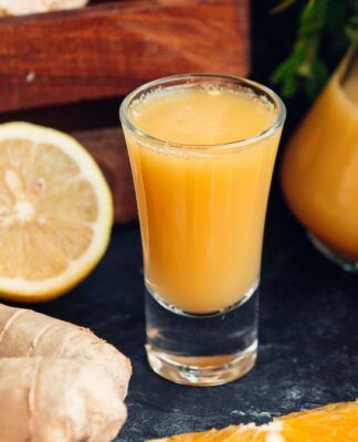 Copo suco de larnaja com laranja e gengibres ao redor