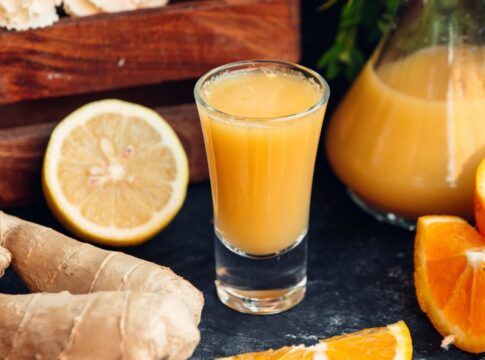 Copo suco de larnaja com laranja e gengibres ao redor