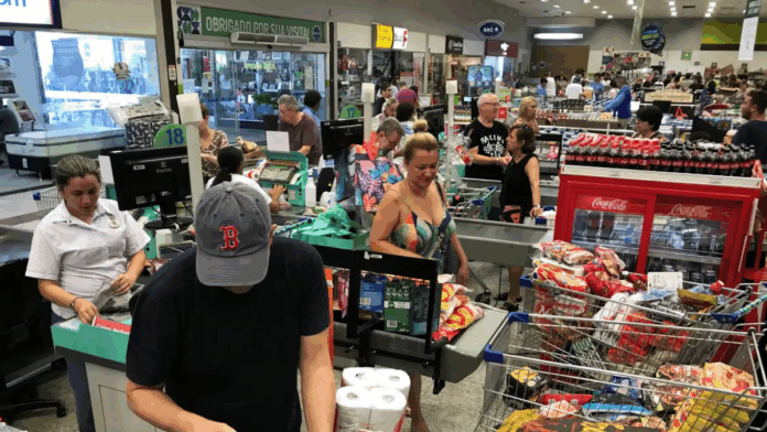 Pessoas em fila de supermercado, com compras.