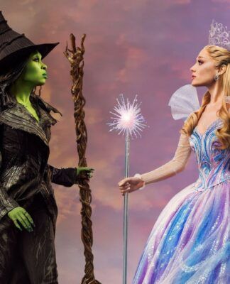 Duas mulheres se encaram em um fundo de céu roxo. Uma mulher segura uma vassoura e é verde. A outra é branca e segura uma varinha.