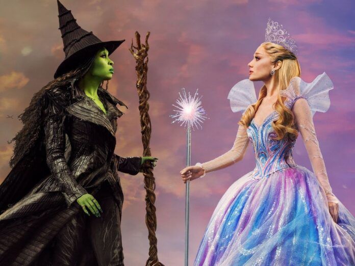 Duas mulheres se encaram em um fundo de céu roxo. Uma mulher segura uma vassoura e é verde. A outra é branca e segura uma varinha.