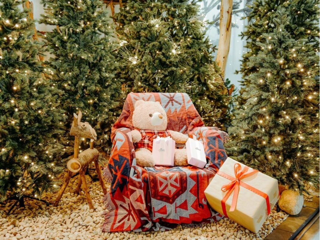 Poltrona com urso de pelúcia e várias árvores natalinas em volta.