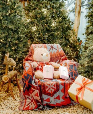 Poltrona com urso de pelúcia e várias árvores natalinas em volta.