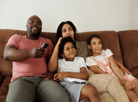 Uma família sentada no sofá assistindo um filme. Um homem está com controle na mão
