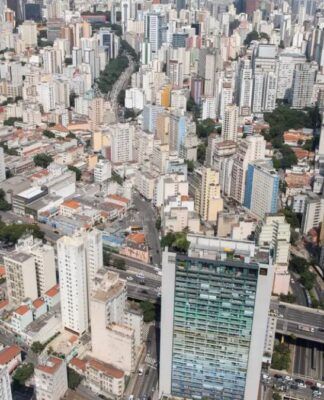 Do alto aparecem casas e diversos prédios da zona central de São Paulo