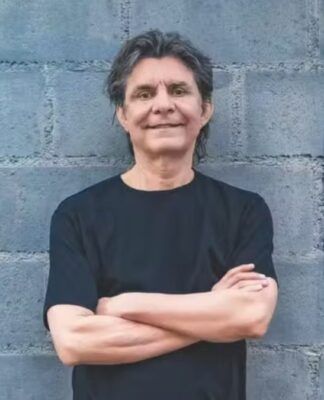 Lô Borges encostado em uma parede de tijolos cinza