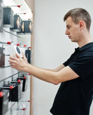 Homem branco e loiro de camiseta preta analisando produtos a venda em uma loja de eletrônicos