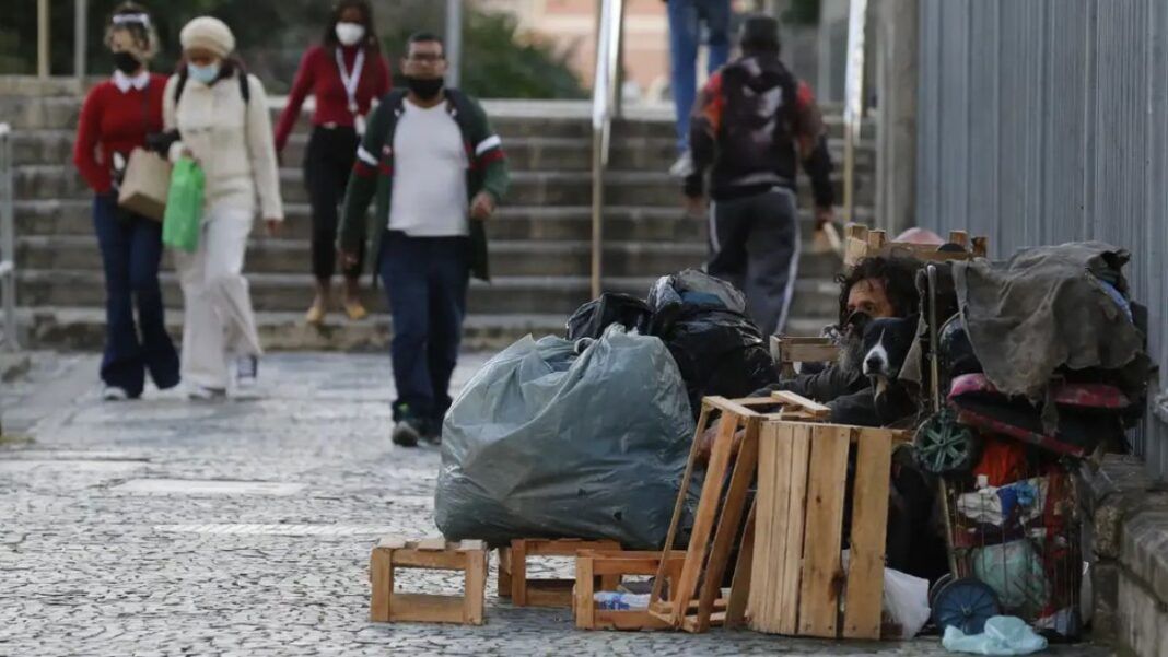 Mulher em situação de rua limpa a entrada de sua barraca