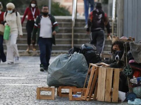 Mulher em situação de rua limpa a entrada de sua barraca