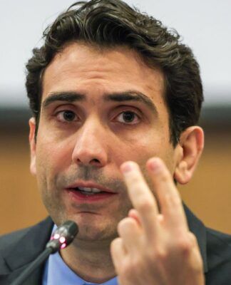 Presidente do Banco Central, Gabriel Galípolo fala ao microfone e faz sinal de número dois com os dedos das mãos esquerda