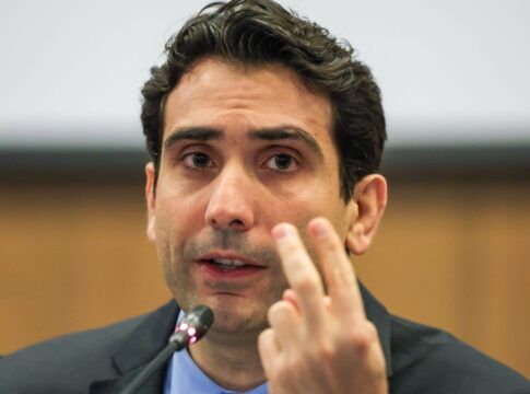 Presidente do Banco Central, Gabriel Galípolo fala ao microfone e faz sinal de número dois com os dedos das mãos esquerda