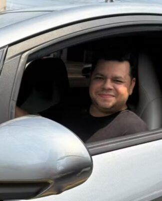 Motorista Alberto dentro de um carro prata, no banco do motorista