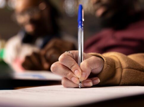 Mão de mulher negra segurando uma caneta azul e redigindo um texto
