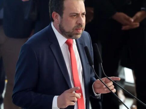 Boulos discursando em um palanque usa ndo terno escuro, camisa branca e gravata vermelha