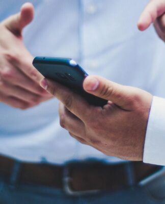 Uma mão segura um celular enquanto outra mão aponta para o aparelho