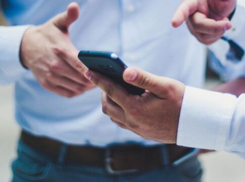 Uma mão segura um celular enquanto outra mão aponta para o aparelho