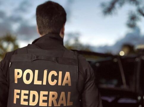 Agente, de costas, apresenta a inscrição polícia federal em seu uniforme