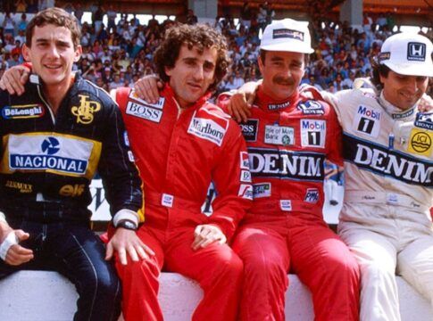 Ayrton Senna, Alain Prost, Nigel Mansell e Nelson Piquet estão sentados numa mureta com seus macacões durante um GP