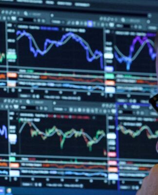 Homem de óculos, ao canto da imagem, analisando uma série de gráficos indicativos de bolsa de valores