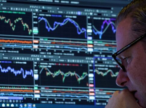 Homem de óculos, ao canto da imagem, analisando uma série de gráficos indicativos de bolsa de valores