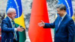 Dois líderes políticos, um do Brasil e outro da China, sorriem e estendem as mãos para um cumprimento diante das bandeiras de seus países.