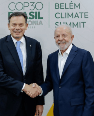 Dois homens de terno sorriem e se cumprimentam com um aperto de mão diante de bandeiras do Brasil e de Portugal, com o painel ao fundo exibindo o texto “COP30 Brasil Amazônia 2025 – Belém Climate Summit”.