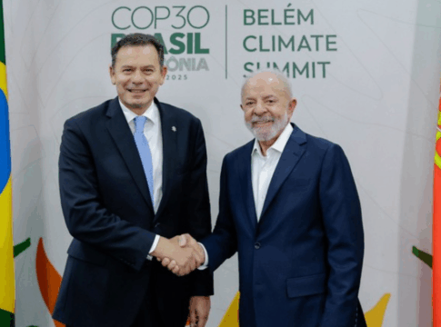 Dois homens de terno sorriem e se cumprimentam com um aperto de mão diante de bandeiras do Brasil e de Portugal, com o painel ao fundo exibindo o texto “COP30 Brasil Amazônia 2025 – Belém Climate Summit”.