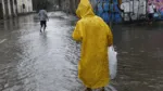 Homem caminha em rua alagada devido a chuva forte