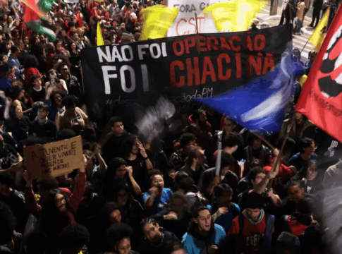 Multidão participa de manifestação à noite segurando faixas e cartazes. Um dos principais cartazes diz “Não foi operação, foi chacina”, e outro, “A juventude quer viver! Parem de nos matar!”. Bandeiras coloridas são erguidas entre os manifestantes.