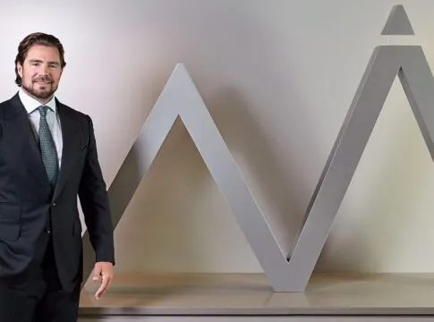 Daniel Vorcaro figura à frente do logo do seu banco vestido de terno e gravata