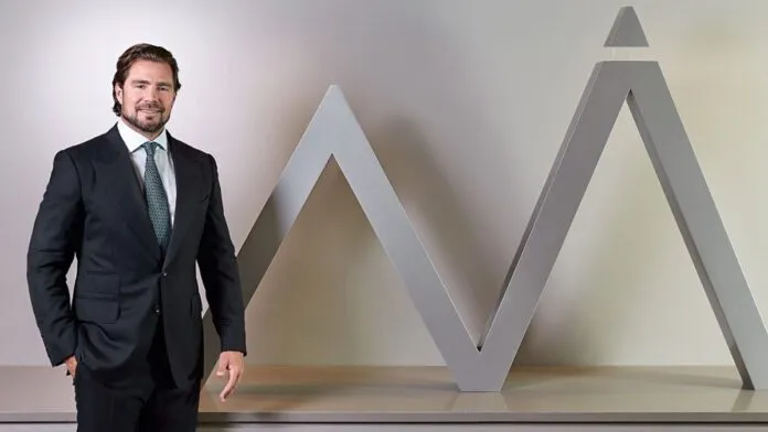 Daniel Vorcaro figura à frente do logo do seu banco vestido de terno e gravata