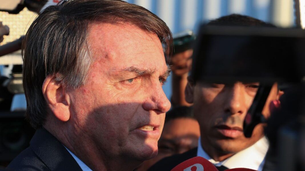 Esta é um close-up lateral do ex-presidente brasileiro Jair Bolsonaro em um ambiente externo, provavelmente falando ou respondendo a jornalistas.