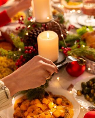 Na foto há uma mesa de jantar em que há muitos pratos, velas e pessoas comendo.